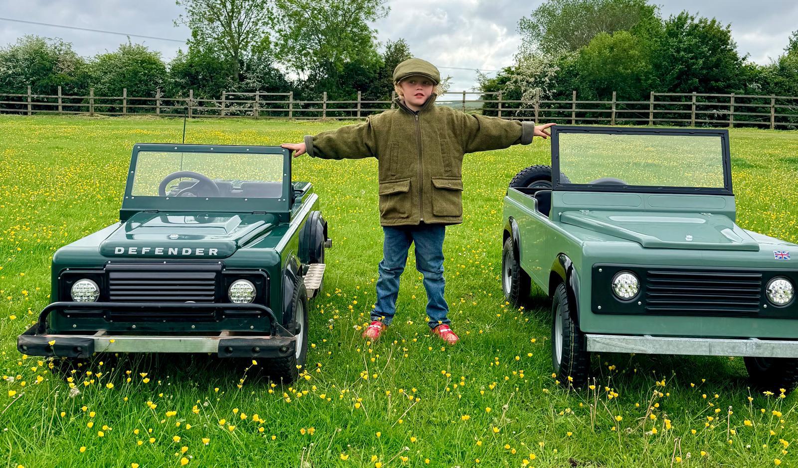 A child standing between both mini Land Rovers in a buttercup meadow