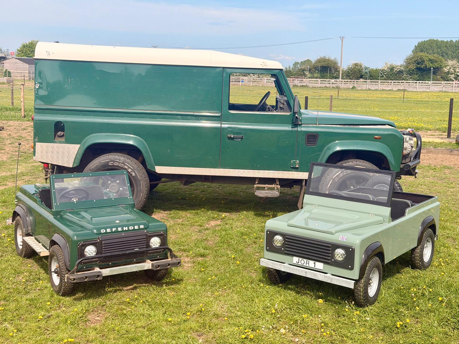 Both mini Land Rovers parked beside a full-size Defender, showing the scale