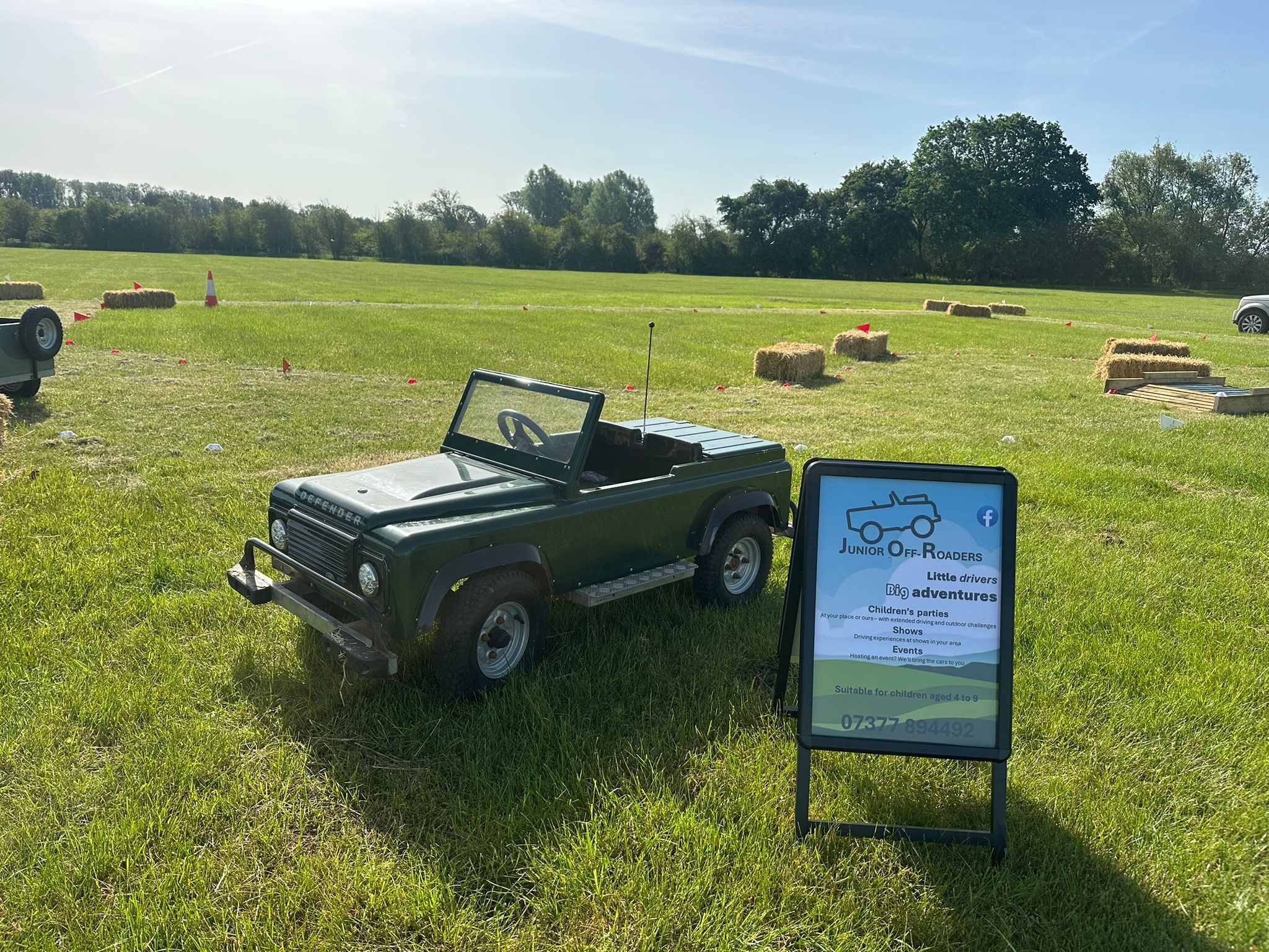 A mini electric Defender Land Rover parked at a country show next to the Junior Off-Roaders sign